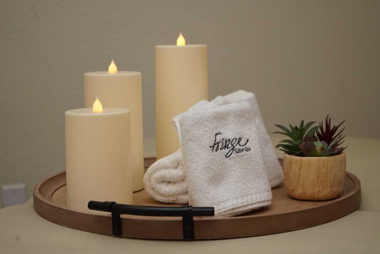 Tranquil spa setup with candles, towels, and a small plant on a wooden tray.